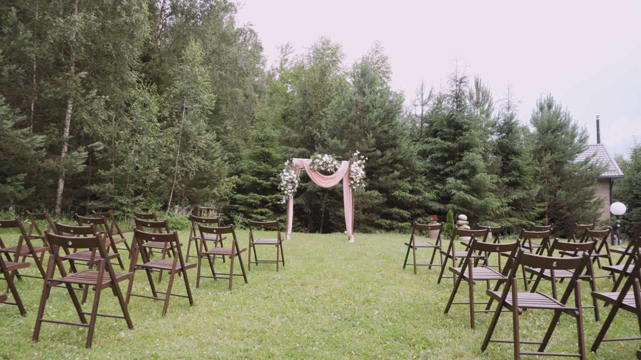 Wooden wedding decorated arch and chairs stands on lawn near forest.