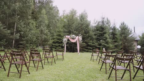 wooden wedding decorated arch and chairs stands on lawn near forest.