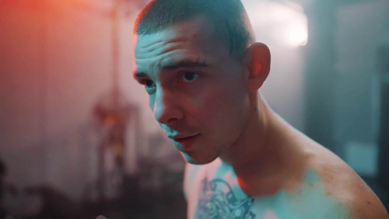Giovane uomo serio con tatuaggio sul petto in una palestra illuminata al neon