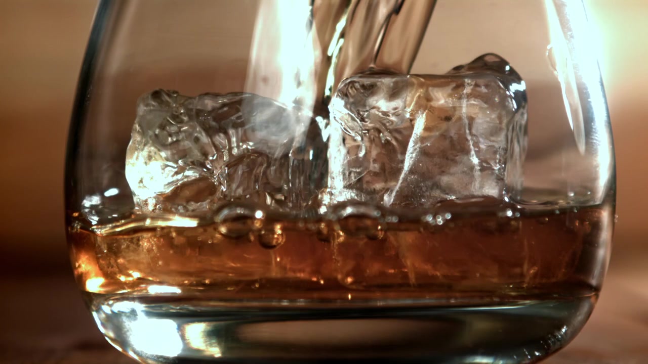Versamento al rallentatore di whisky dorato in un bicchiere con ghiaccio
