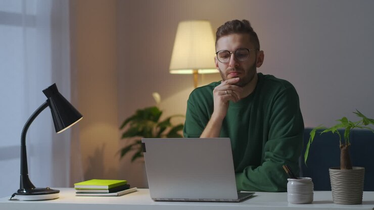 giovane pensieroso è seduto a tavola con il portatile scrittore o giornalista sta lavorando su un libro in casa medio ritratto agonie interne della creazione