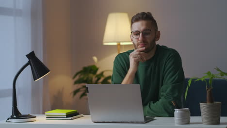 Nachdenklicher-Junger-Mann-Sitzt-Mit-Laptop-Am-Tisch,-Schriftsteller-Oder-Journalist-Arbeitet-Zu-Hause-An-Einem-Buch,-Mittleres-Porträt-Im-Innenbereich,-Wehen-Der-Schöpfung