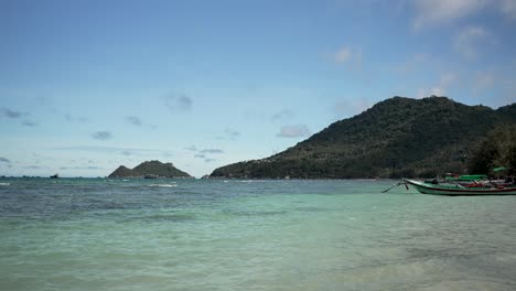 태국 코타오 (koh tao) 의 아름다운 해변 풍경은 은 푸른 물, 울창한 초록색 언덕, 그리고 조용한 파란 하늘 아래의 전통적인 배를 보여줍니다.