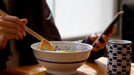 Mujer-Comiendo-Fideos-Mientras-Usa-El-Teléfono-Móvil-En-El-Restaurante-4k