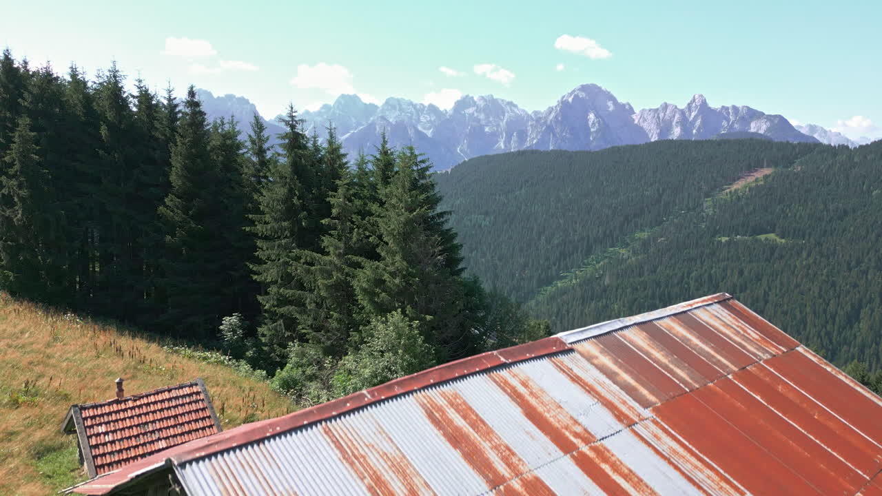 video de drones que se eleva lentamente verticalmente desde detrás del antiguo granero de la granja en la histórica ciudad de la ladera para revelar el bosque y la cordillera en el fondo en un día soleado en verano en los dolomitas italia