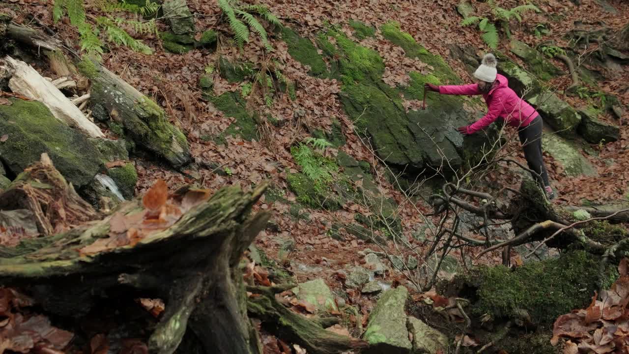 Girl walking down a hiking trail with fall colour leaves on the ground. Lady holding on to the rocks for balance in the winter. Waterfall of Veliki Sumik in the eastern part of Slovenia