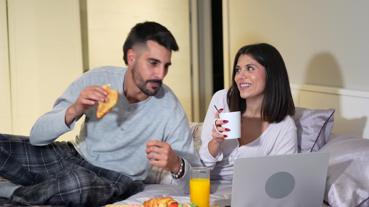Couple Enjoying Breakfast in Bed with Laptop