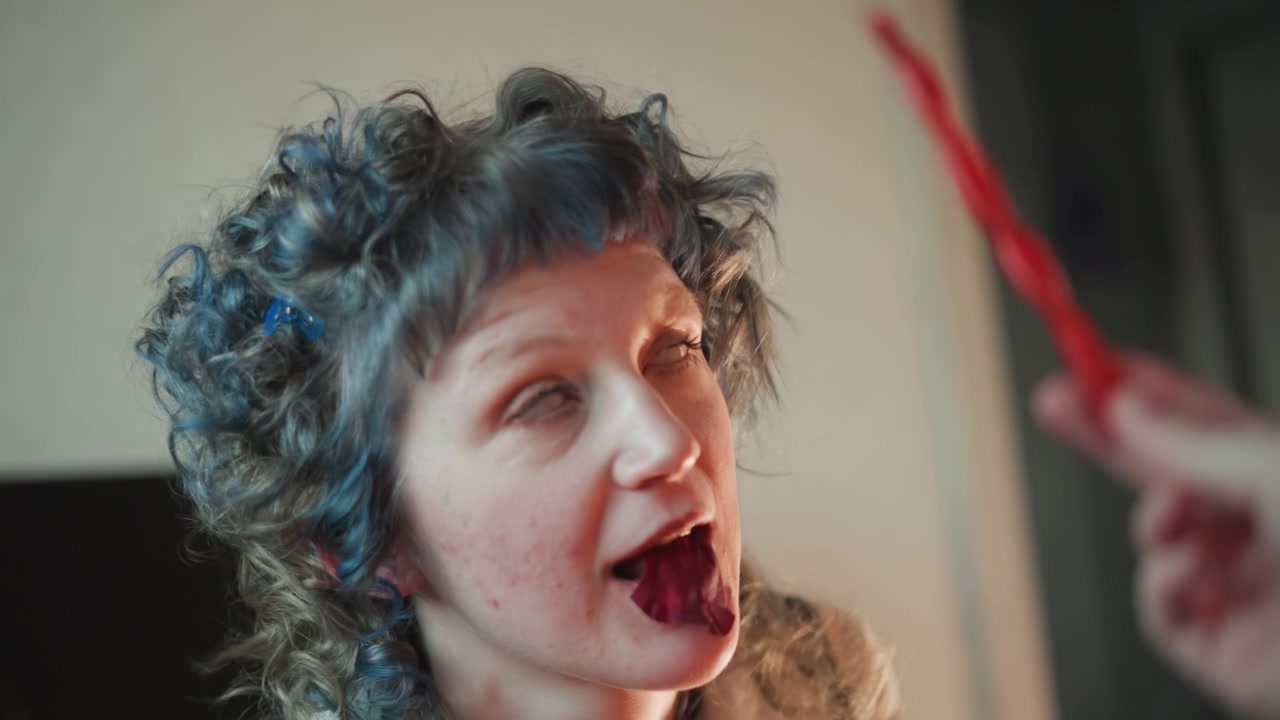 Lips and hands. Fun moment of woman sampling red candle with laughter indoors. Indoor scene showing woman with curly hair enjoying ritual wax with joyful expression and textured details