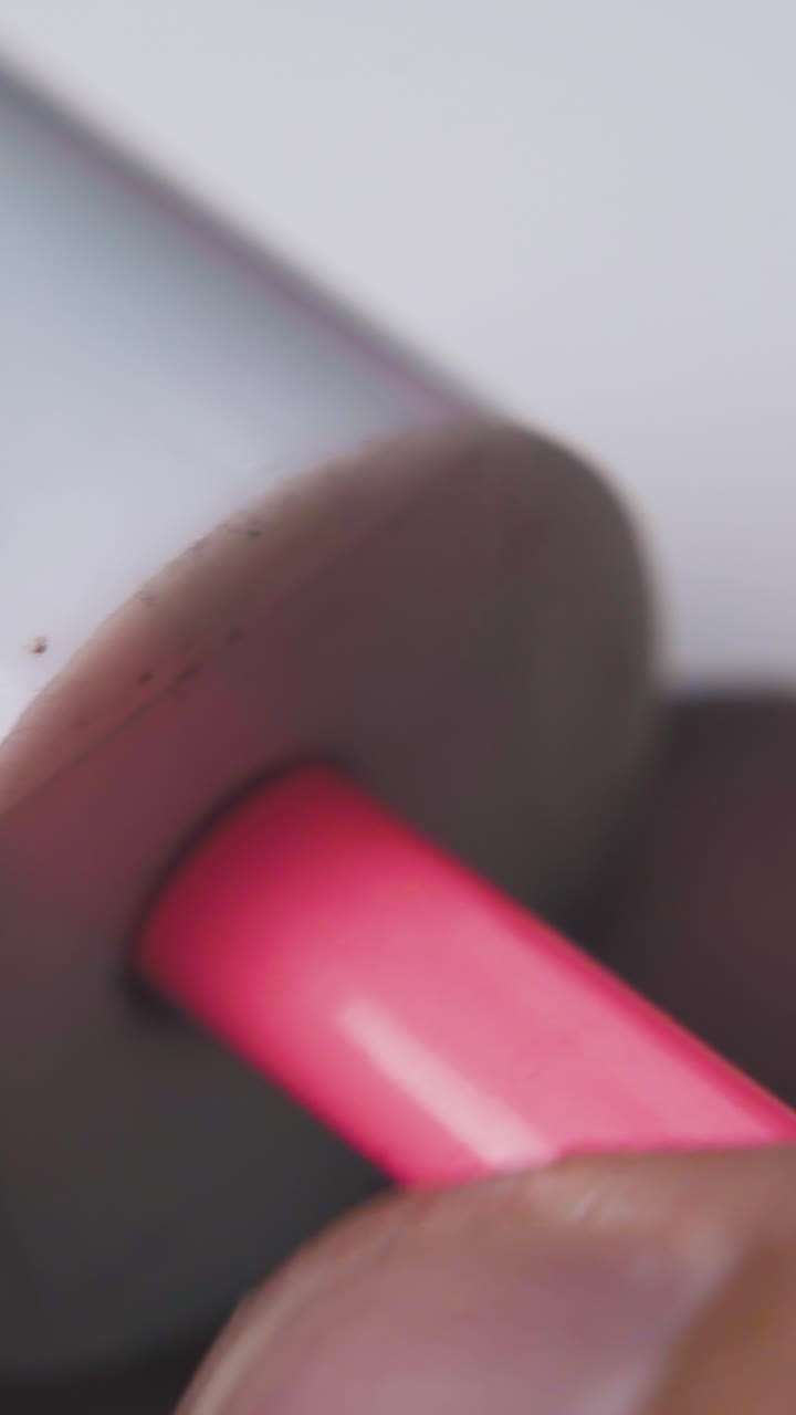 man turns bright pink pencil holding white plastic sharpener in fingers on light background extreme close view