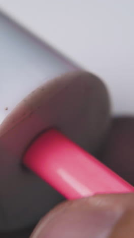 man turns bright pink pencil holding white plastic sharpener in fingers on light background extreme close view