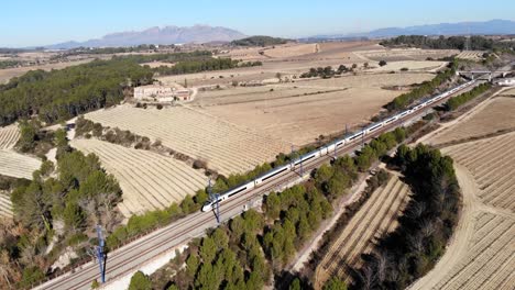 aerial: high-speed train in spain, travelling between barcelona and madrid, in the catalan countryside and montserrat mountain range in the blackground