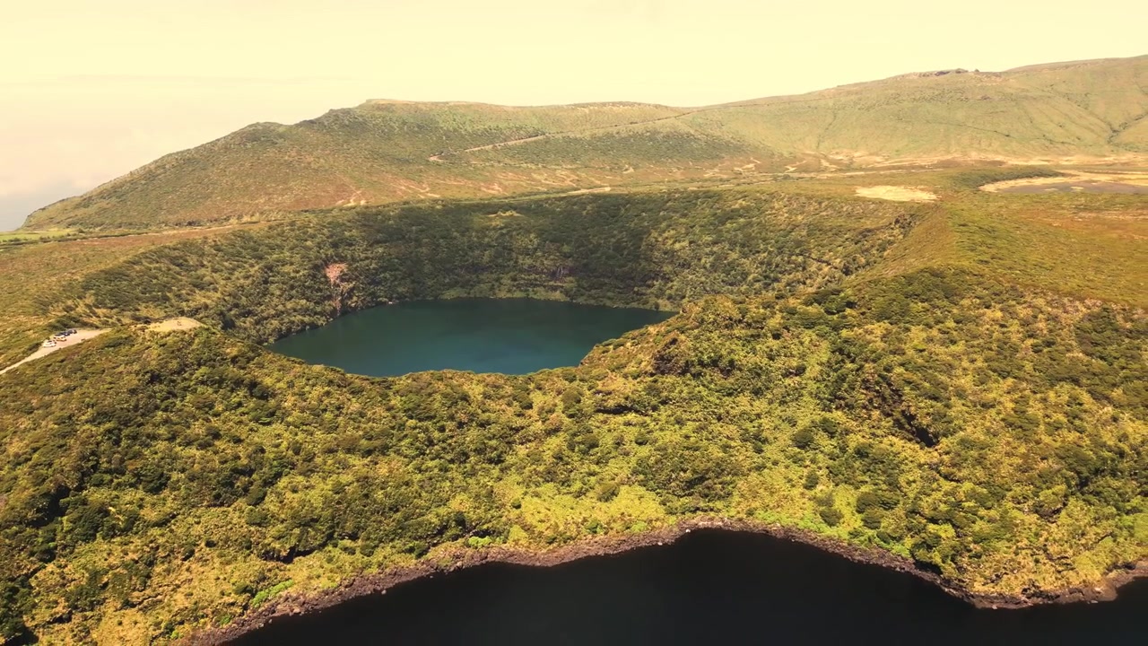 Vista aérea sobrevoa exuberante lago de cratera vulcânica cercado por colinas verdes na ilha das Flores.