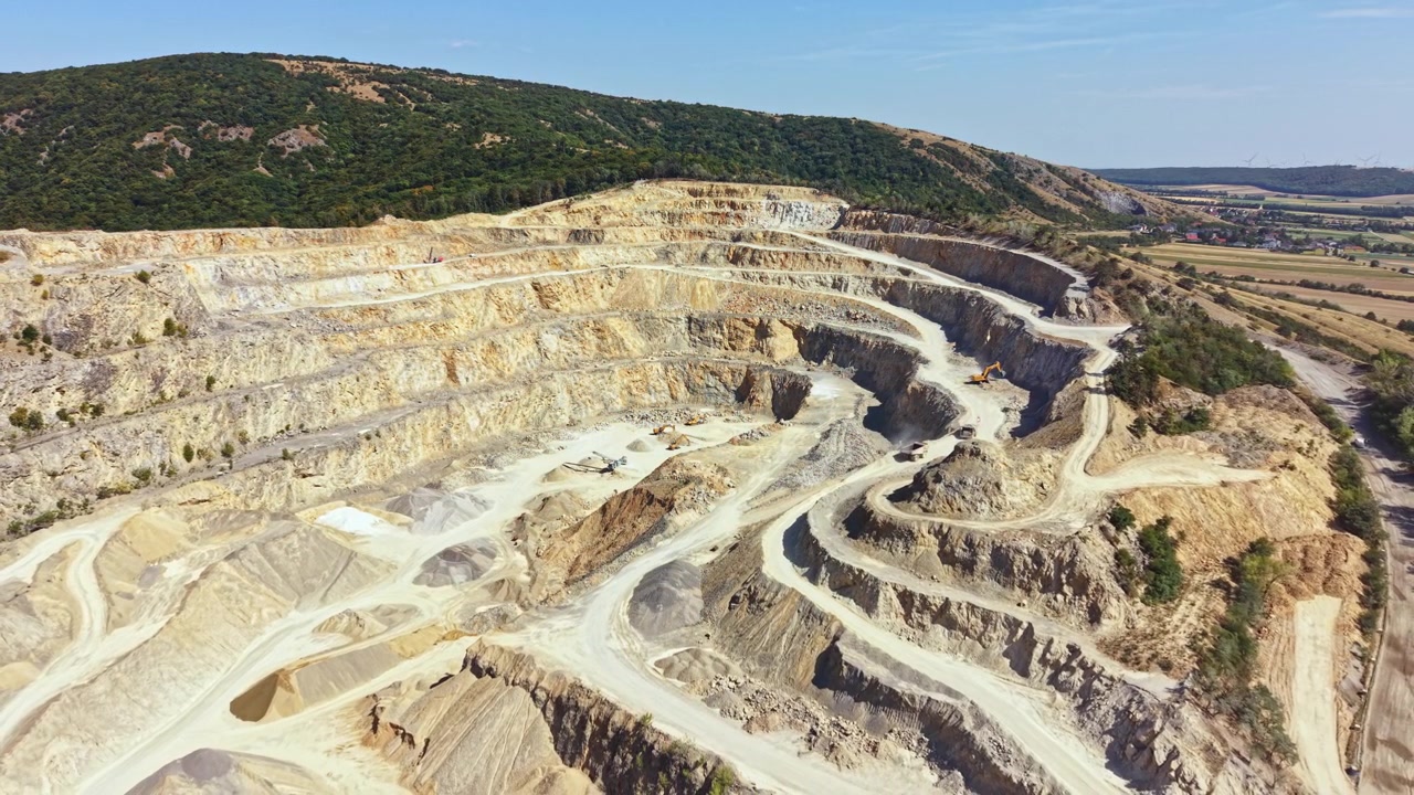 Large open pit mine located in a hilly area showing layers of rock and earth for mineral extraction