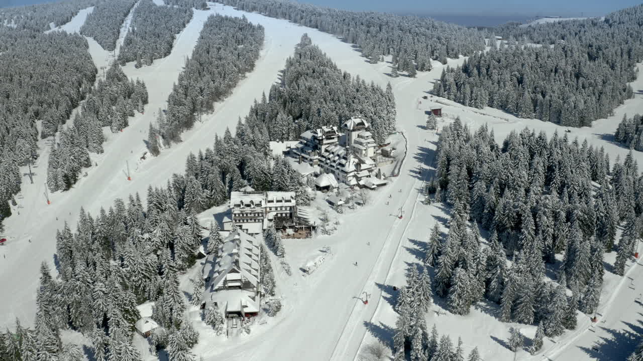 Aerial view of a snow-covered ski resort with hotels, ski slopes, and pine trees in the mountains