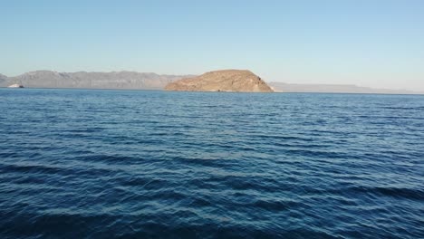 Flying-over-the-blue-waters-of-the-Sea-of-Cortez-with-a-drone,-near-Playa-El-Coyote,-BCS,-Mexico,-the-island-coyote-in-the-distance