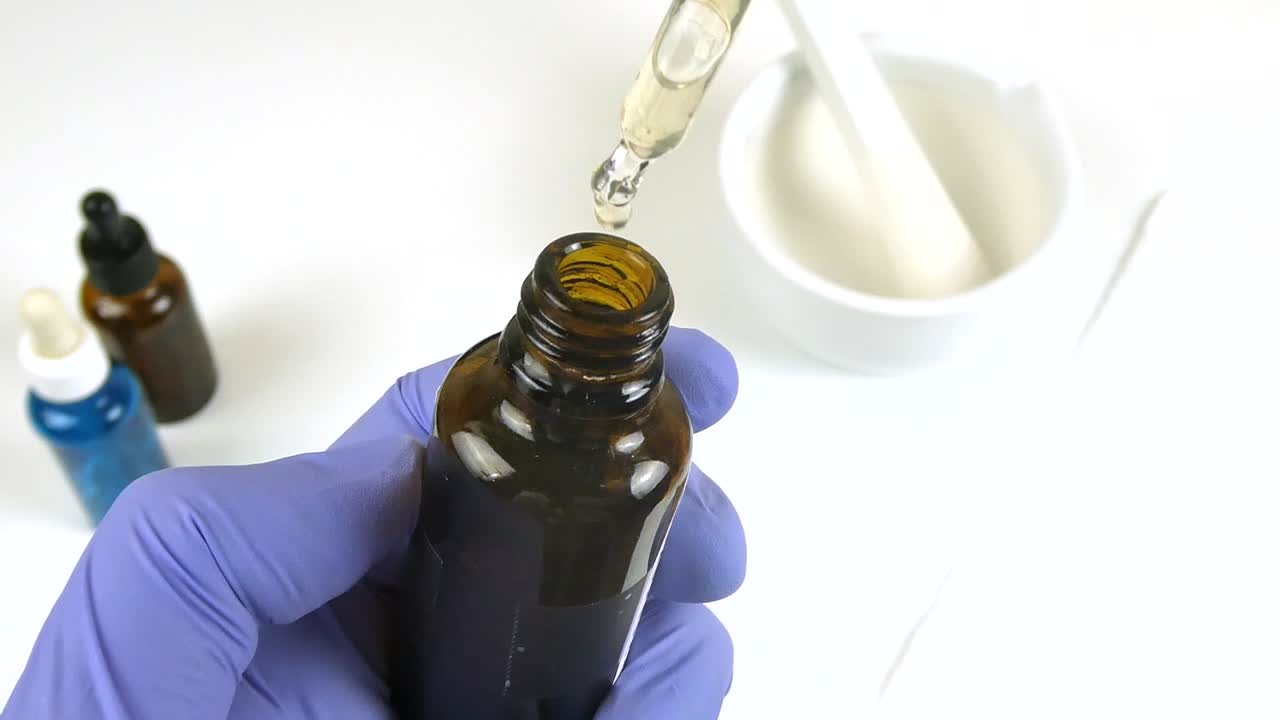 Pharmacist's gloved hand dropping cosmetic serum into a bottle with a mortar and pestle nearby