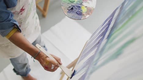 video of midsection of biracial female artist painting in studio