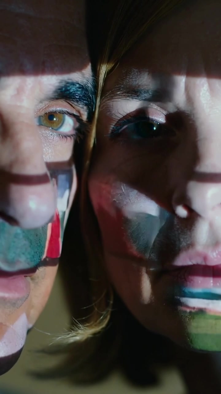 Video vertical: Proyectando luz con patrones que se mueve sobre dos rostros en una habitación tenue, creando arte de color.