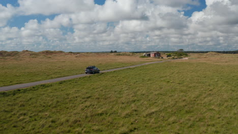 Verfolgung-Von-Autofahrten-Auf-Der-Straße-Auf-Dem-Land.-Vorbei-An-Einem-Anderen-Auto-Und-Einem-Schönen-Bewaldeten-Ferienhaus.-Flache-Wiesen.-Dänemark