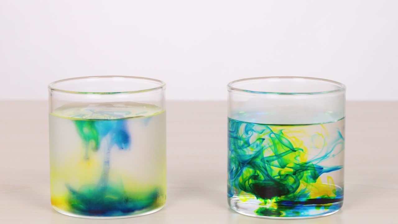 Blue and yellow dye disperses in clear water, forming swirling patterns under bright, even lighting