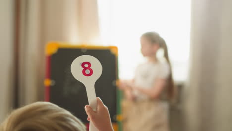 Little-boy-shows-digit-on-plastic-tag-with-sister-at-home