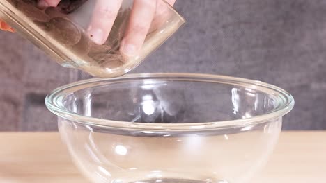 close-up of chocolate discs being poured into a clear glass bowl on a wooden surface.