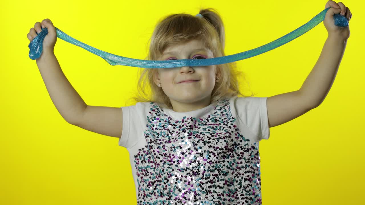 손으로 만든 장난감 슬림으로 놀고 있는 아이. 슬림을 만드는 재미를 느끼는 어린 소녀. 노란색 배경