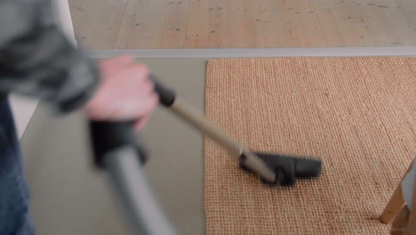 young male using a vacuum cleaner on a carpet at home