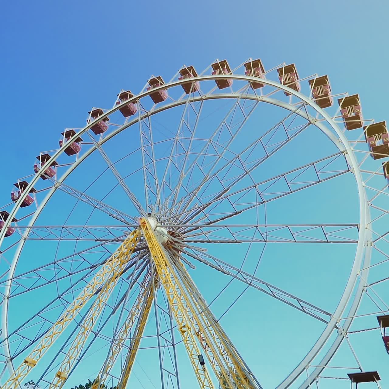 Ferris wheel with colorful gondolas. Blue sky and sunny day in amusement park