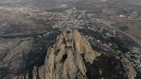 Vista-Aérea-De-La-Peña-De-Bernal,-Pico-De-La-Montaña-Con-El-Pueblo-De-Bernal-Al-Fondo-En-Querétaro,-México