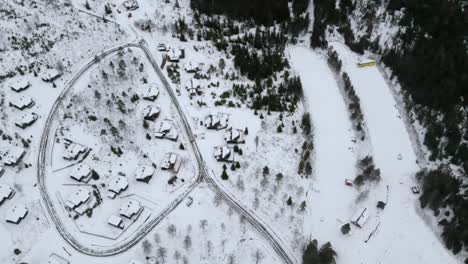 Toma-De-Drone-De-Un-Pequeño-Pueblo-De-Cabañas-En-Una-Pendiente-Con-Nieve.