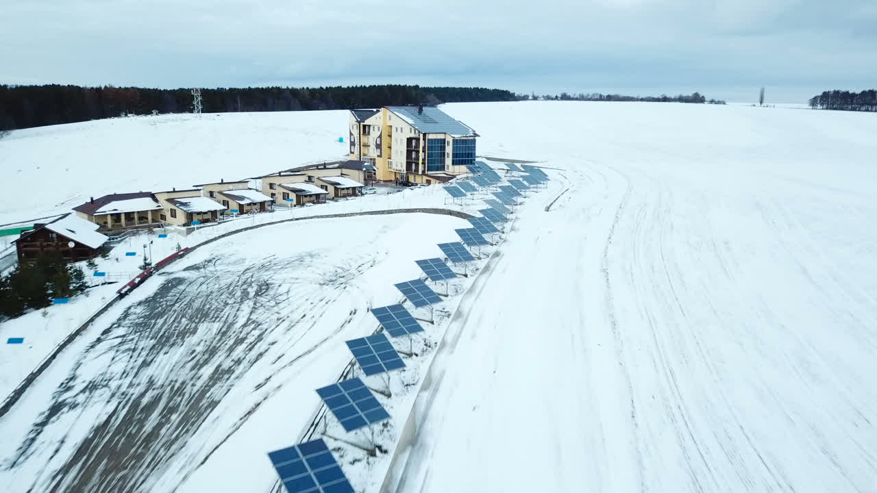 Hotel complex in the mountains with solar panels on the snow. Rows of snow covered solar panels in a small solar power plant.