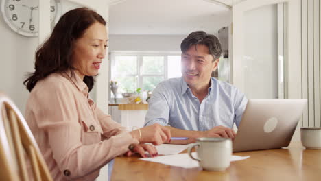 Mature-Asian-couple-sitting-at-table-at-home-using-laptop-to-organise-household-bills-and-finances---shot-in-slow-motion