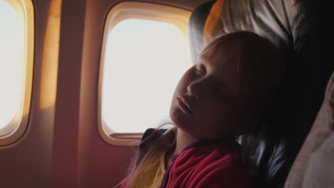 the little girl is sleeping in the cabin of the plane. during the dawn, the orange rays of the sun illuminate her face