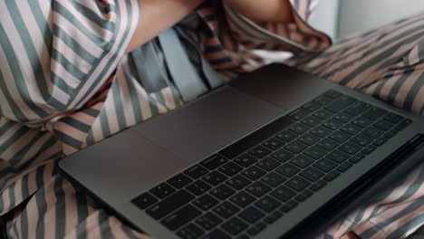 Freelancer-working-laptop-computer-in-pajamas-closeup.-Woman-watch-online-blog
