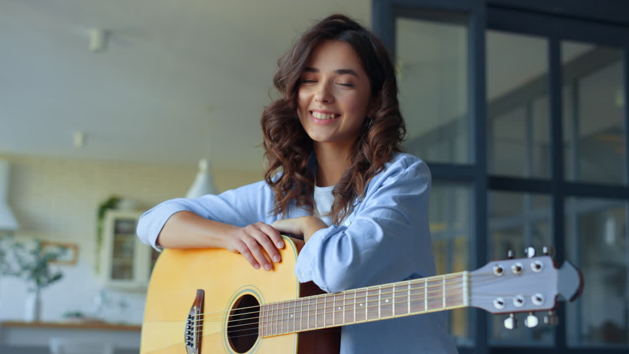 Ragazza sognante che tiene in mano una chitarra acustica a casa. Donna felice che guarda la fotocamera
