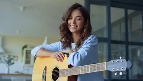 Dreamy-girl-holding-acoustic-guitar-at-home.-Happy-woman-looking-at-camera
