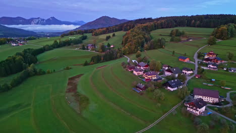 Aerial-drone-forward-moving-shot-over-village-houses-surrounded-by-green-farmlands-along-hilly-terrain-at-daytime