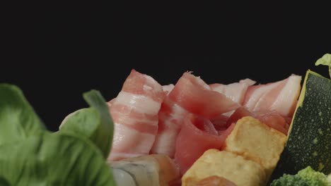 close up of a pot of shabu ingredients spinning around on the black background