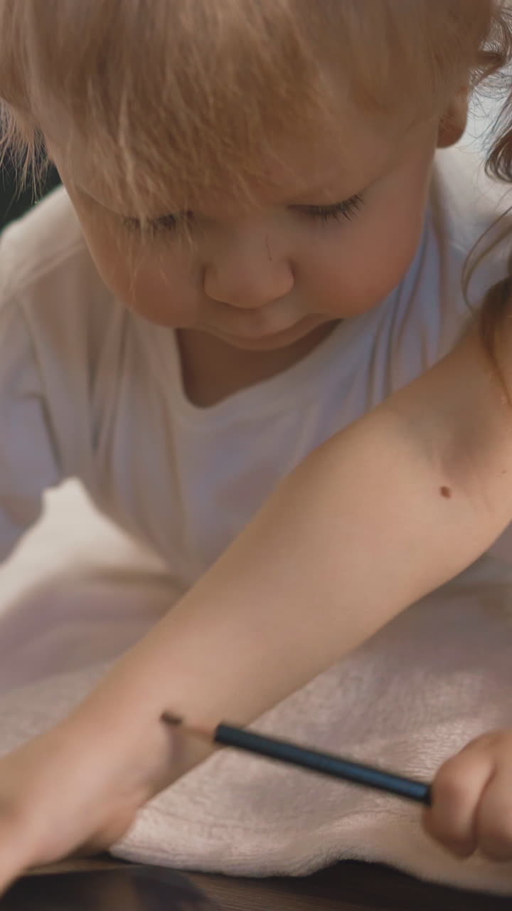 cu, low angle shot: little blond toddler lies on floor with smartphone, smiles, girl, sister of child, strokes his head with his hand, picks up mobile phone closeup