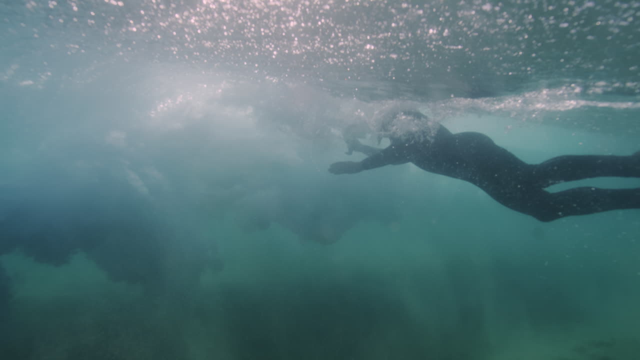Underwater view of a photographer swimming and chasing backside of vortex in shorebreak with sand churning up in clear Australian waters