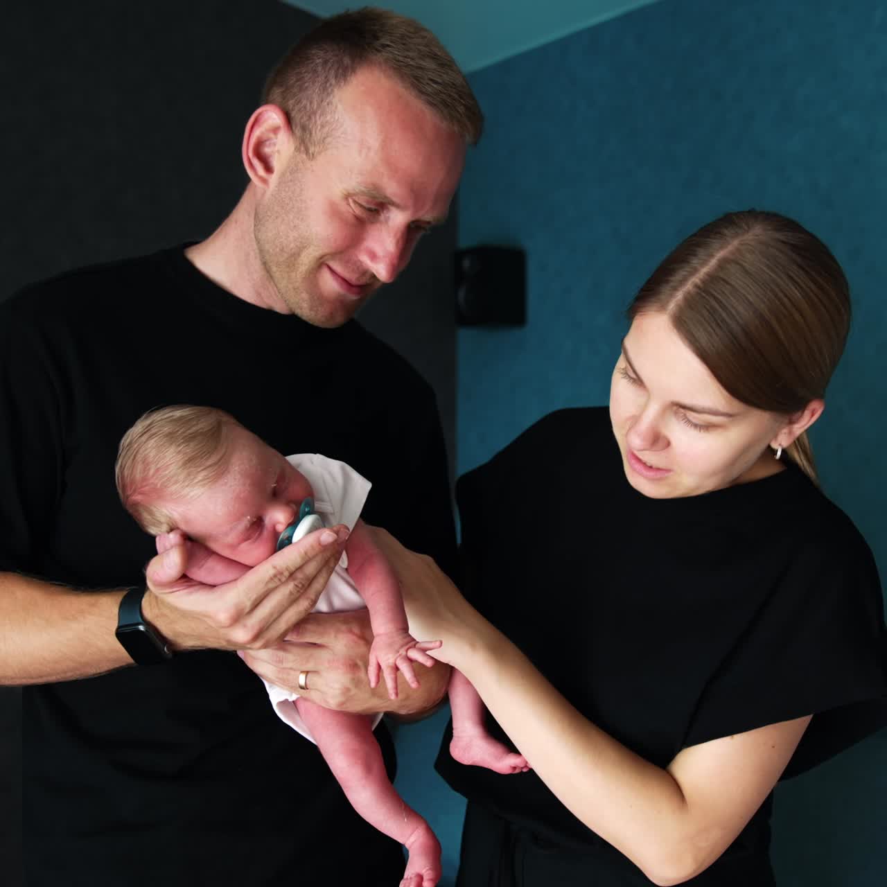 New-made parents wearing black t-shirts holding a tiny sleeping newborn. Family on the first day of baby life