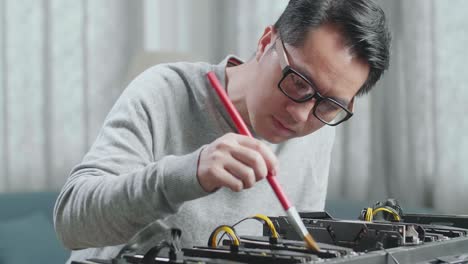 안경을 쓴 아시아 남자가 암호화폐를 채굴하기 위해 광산 기계를 청소합니다.