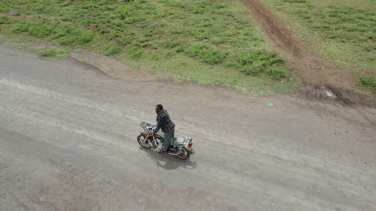 hombre montando motocicleta en camino de tierra en áfrica realizando acrobacias, loitokitok, kenia, vista aérea