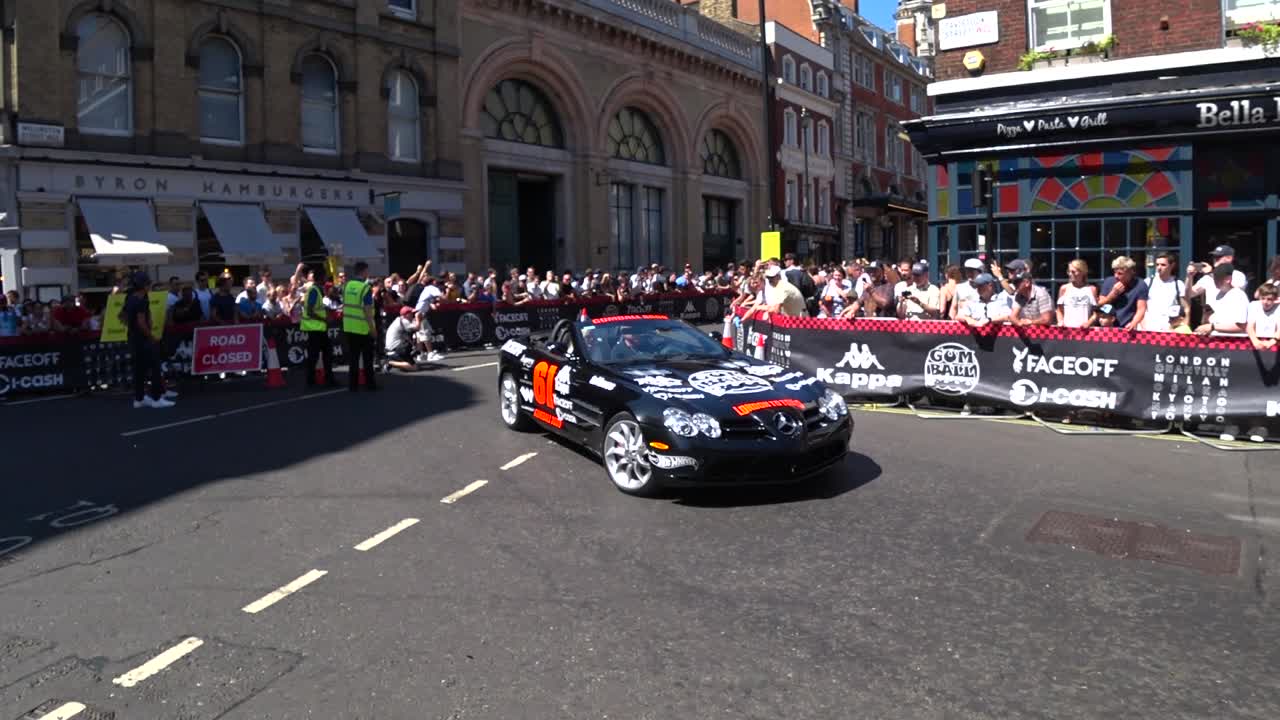 Static medium shot of luxury cars driving on London Roads during sunny day with many spectators on the roadside. Gumball 3000 London.