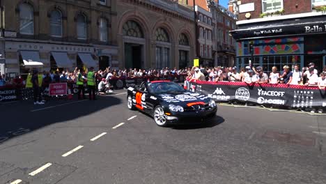 static medium shot of luxury cars driving on london roads during sunny day with many spectators on the roadside. gumball 3000 london.