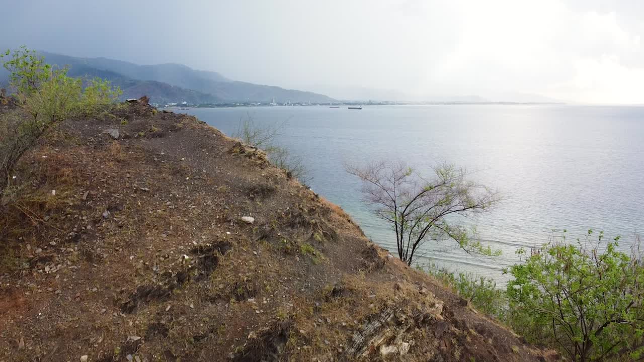 Aerial rising view overlooking white sandy beach and ocean with rugged mountains in capital city of Dili, Timor-Leste, Southeast Asia