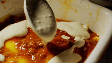 placing white milk and cream sauce on top of a homemade european lasagne food