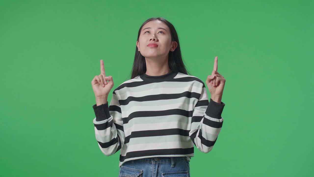 Asian Woman Pointing Up While Standing In Front Of Green Screen Background