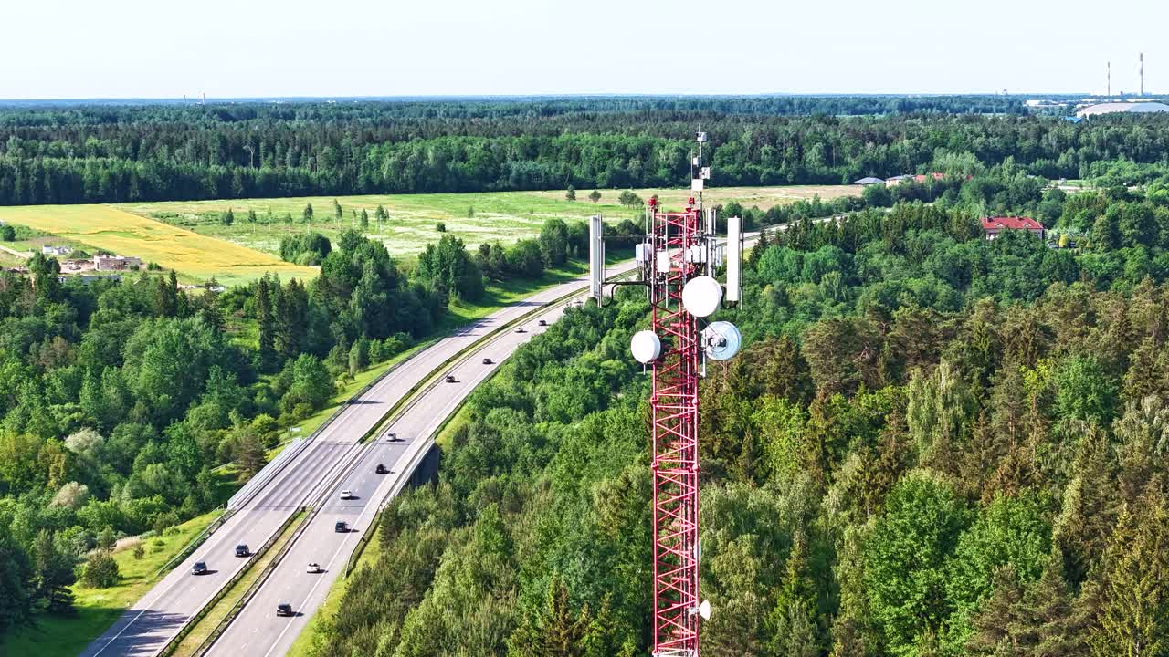 5G cell antenna tower with green forest and highway, aerial time lapse view